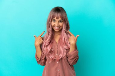 Mavi arka planda izole edilmiş pembe saçlı melez bir kadın baş parmak işareti yapıyor.
