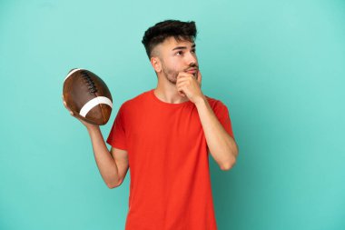 Rugby oynayan genç beyaz adam mavi arka planda izole edilmiş ve yukarı bakıyor.