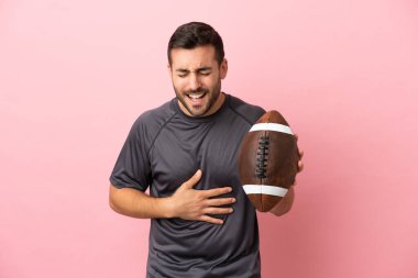 Genç, beyaz bir adam pembe arka planda izole edilmiş rugby oynarken gülümsüyor.