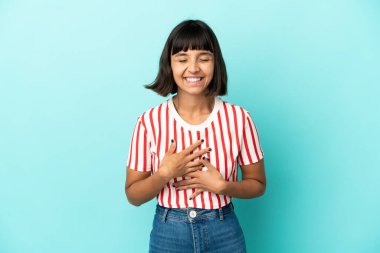 Genç melez kadın mavi arka planda izole edilmiş, çok gülümsüyor.