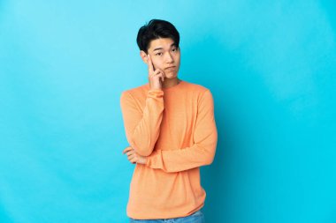 Genç Çinli bir adam mavi arka planda izole edilmiş bir fikir düşünüyor.