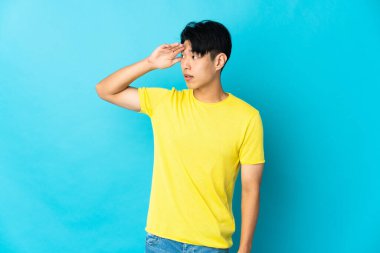 Mavi arka planda mahsur kalmış genç Çinli bir adam sürpriz bir ifadeyle yan tarafa bakıyor.