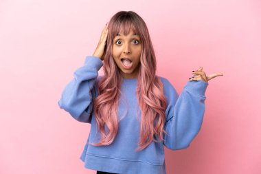 Pembe saçlı melez bir kadın. Pembe arka planda izole edilmiş. Şaşırmış ve işaret ediyor.