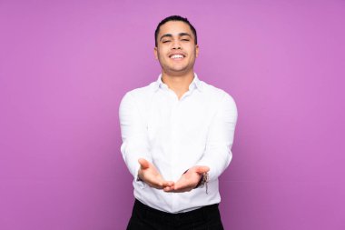 Asyalı yakışıklı bir adam mavi arka planda izole edilmiş. Avucunun içinde hayali bir ilan tutuyor.