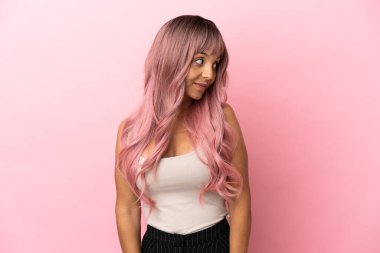 Pembe saçlı genç melez kadın pembe arka planda izole edilmiş şüpheli hareketler yapıyor.