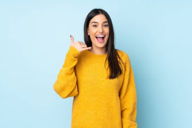 Mavi arka planda izole edilmiş beyaz bir kadın telefon jesti yapıyor. Bana geri dönüş işareti ver.