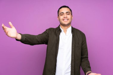 Asyalı yakışıklı adam mavi arka planda izole edilmiş sunar ve davet eder.