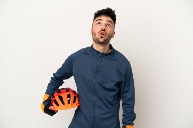 Genç bisikletçi beyaz arka planda izole edilmiş yukarı bakıyor ve şaşırmış bir ifadeyle