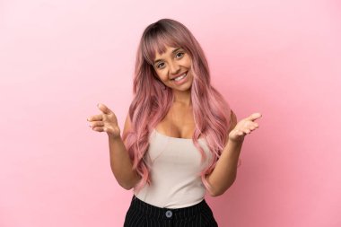 Pembe saçlı genç melez kadın pembe arka planda izole edilmiş sunar ve davet eder.