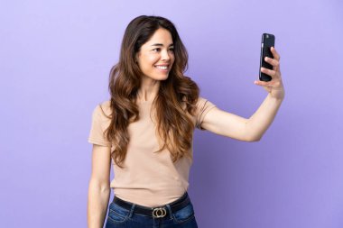 Woman over isolated purple background making a selfie