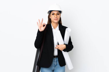 Miğferli, beyaz, genç bir kadın izole edilmiş arka planda elinde planlar var. Parmaklarıyla iyi bir işaret gösteriyor.