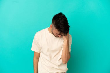 Kafkasyalı genç adam mavi arka planda izole edilmiş, baş ağrısı var.