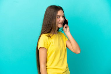 Küçük kız izole edilmiş mavi arka planda cep telefonuyla sohbet ediyor.