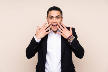 Asyalı iş adamı, bej arka planda yalıtılmış, şaşırmış yüz ifadesi var.