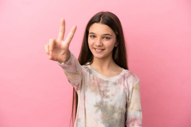 Küçük kız pembe arka planda gülümsüyor ve zafer işareti gösteriyor.