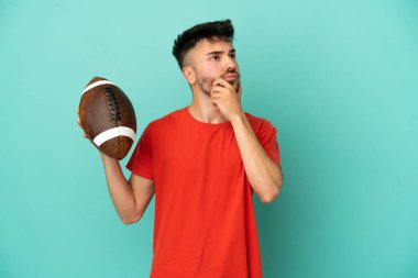 Rugby oynayan Kafkasyalı genç adam mavi arka planda izole edilmiş. Şüpheleri var.