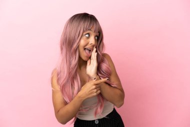 Pembe arka planda pembe saçlı melez bir kadın bir ürünü sunmak ve bir şeyler fısıldamak için kenarı işaret ediyor.