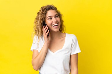 Sarı arka planda izole edilmiş cep telefonu kullanan genç sarışın kadın yukarı bakarken bir fikir düşünüyor.