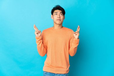 Genç Çinli adam mavi arka planda izole edilmiş, şans diliyor ve en iyisini diliyor.