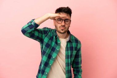 Pembe arka planda izole edilmiş genç beyaz bir adam bir şeye bakmak için çok uzaklara bakıyor.