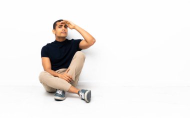 Afro-Amerikalı bir adam yerde oturuyor. Uzaktan bir şeye bakıyor.