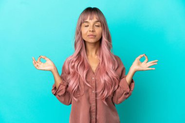 Pembe saçlı, melez bir kadın. Mavi arka planda, zen pozunda.