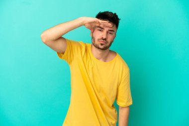 Kafkasyalı genç bir adam mavi arka planda izole edilmiş. Bir şeye bakmak için uzaklara bakıyor.