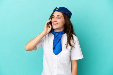 Uçak hostesi kadın mavi arka planda izole edilmiş cep telefonuyla sohbet ediyor.