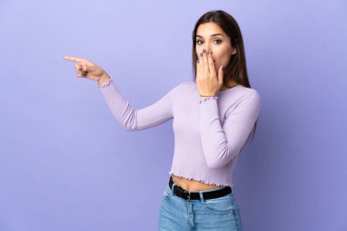 İzole edilmiş arka planda genç beyaz kadın sürpriz bir ifadeyle işaret ederken...