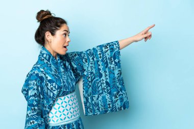 Woman wearing kimono over isolated background pointing away