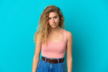 Mavi arka planda yalnız, üzgün bir ifadeyle genç sarışın kadın.