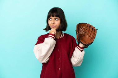 Beyzbol eldivenli genç melez kadın. Mavi arka planda izole edilmiş. Şüpheleri ve düşünceleri var.