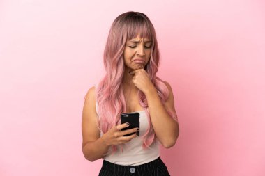 Pembe saçlı melez bir kadın. Pembe arka planda izole edilmiş. Düşünüyor ve mesaj yolluyor.