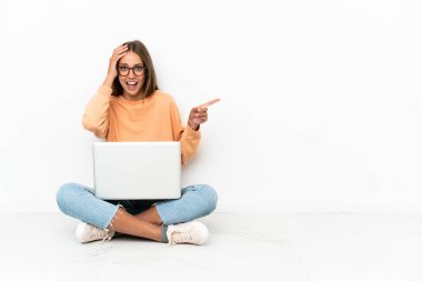 Dizüstü bilgisayarı olan genç bir kadın yerde oturuyor. Şaşırmış ve işaret ediyor.