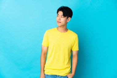 Mavi arka planda izole edilmiş genç bir Çinli yan tarafa bakıyor.