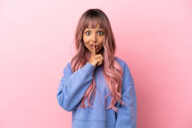 Pembe saçlı melez bir kadın. Pembe arka planda izole edilmiş. Parmağını ağzına koyduğunda sessizlik işareti gösteriyor.
