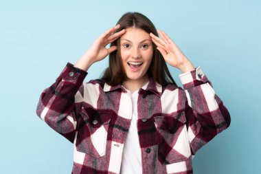 Beyaz kız, mavi arka planda, sürpriz bir ifadeyle izole edilmiş.