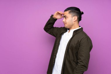 Asyalı yakışıklı adam mavi arka planda mahsur kalmış, sürpriz bir ifadeyle yan tarafa bakıyor.