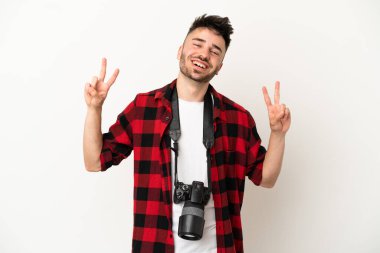 Beyaz arka planda izole edilmiş genç fotoğrafçı iki eliyle zafer işareti gösteriyor.
