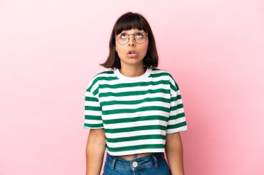 Genç melez kadın pembe arka planda izole edilmiş yukarı bakıyor ve şaşırmış bir ifadeyle