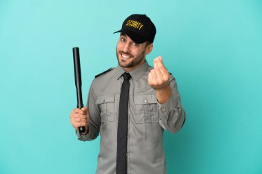 Genç güvenlik görevlisi mavi arka planda izole edilmiş para hareketi yapıyor.