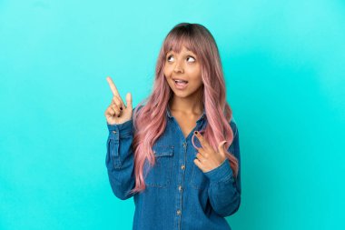 Mavi arka planda izole edilmiş pembe saçlı melez bir kadın işaret parmağıyla işaret etmek harika bir fikir.