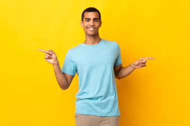 İzole edilmiş arka planda yaşayan Afro-Amerikalı adam parmak uçlarını işaret ediyor ve mutlu.