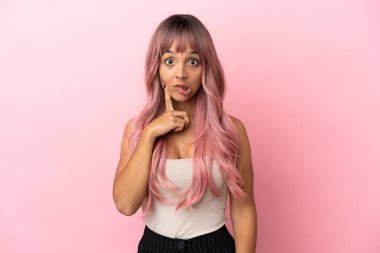 Pembe saçlı melez bir kadın pembe arka planda izole edilmiş ve düşünüyor.