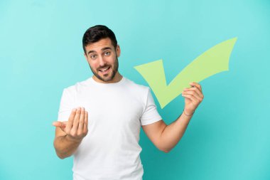 Mavi arka planda izole edilmiş yakışıklı beyaz bir adam elinde bir çek ikonu tutuyor ve bir jest yapıyor.