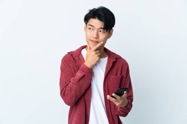 Genç Çinli adam beyaz arka planda cep telefonu ve düşünce kullanarak izole edildi.