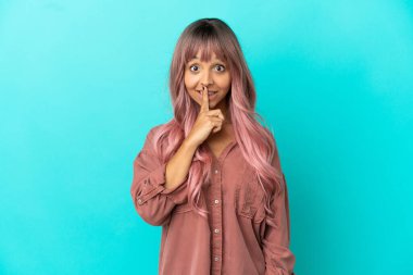 Mavi arka planda izole edilmiş pembe saçlı melez bir kadın sessiz bir jest işareti gösteriyor. Parmağını ağzına sokuyor.