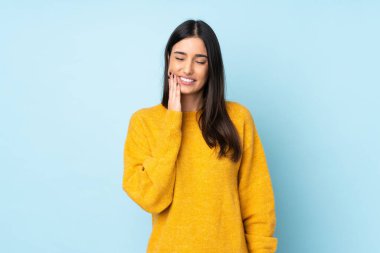 Mavi arka planda diş ağrısı çeken genç beyaz bir kadın.