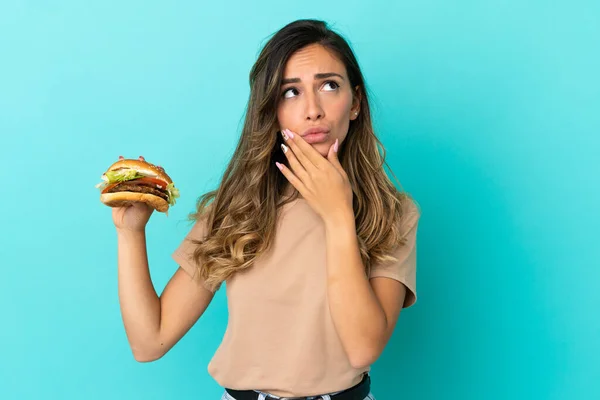 Young Woman Holding Burger Isolated Background Having Doubts — Stock Photo, Image