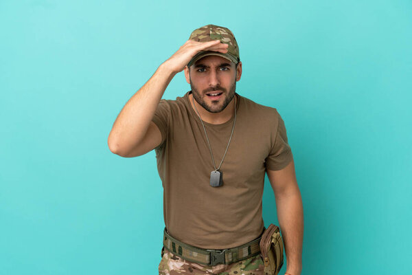 Military with dog tag over isolated on blue background looking far away with hand to look something